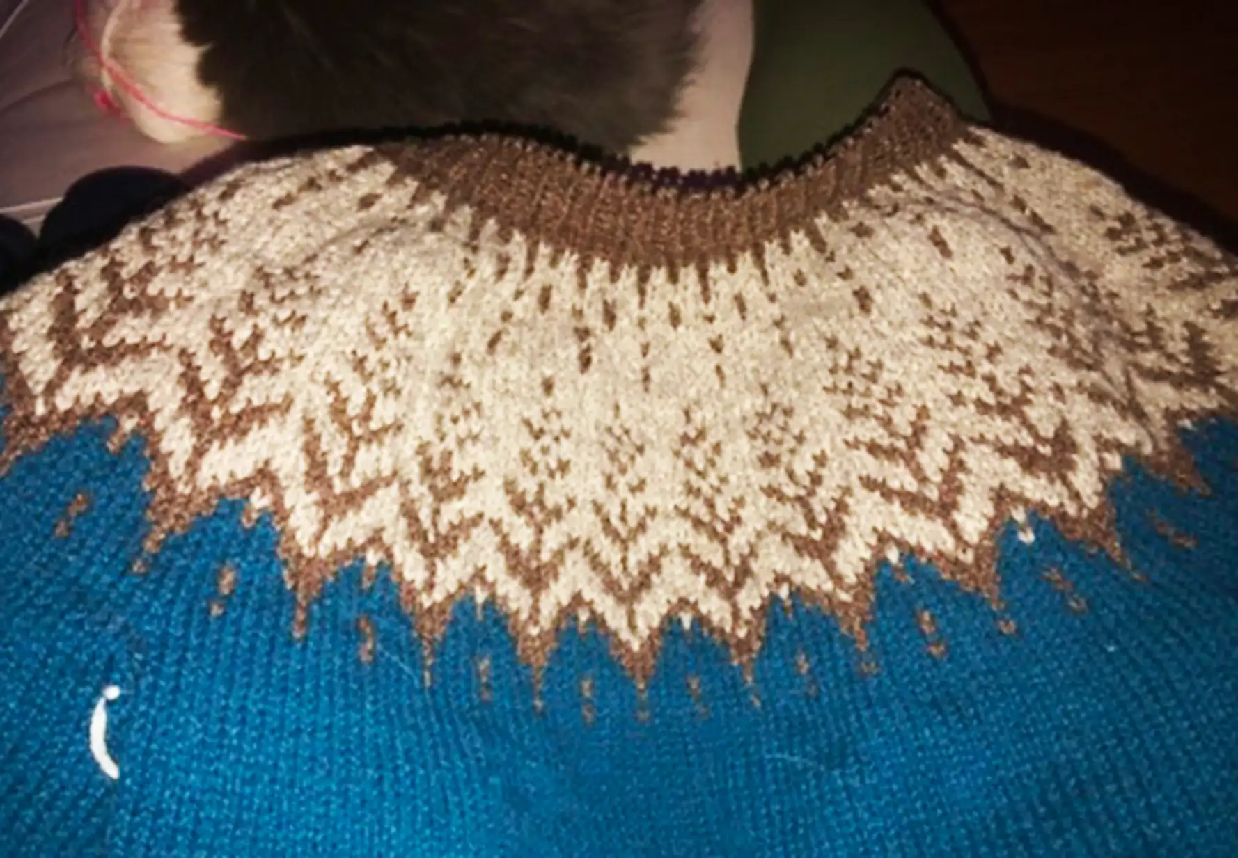 close up of a knitted sweater yoke. the yoke is light beige with brown trees. the sweater is medium teal blue colour